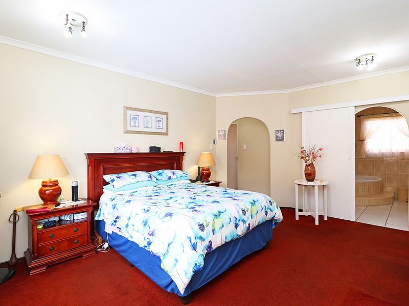 Spacious bedroom featuring red carpeting, an arched entryway, and direct access to an en-suite bathroom through a sliding door.