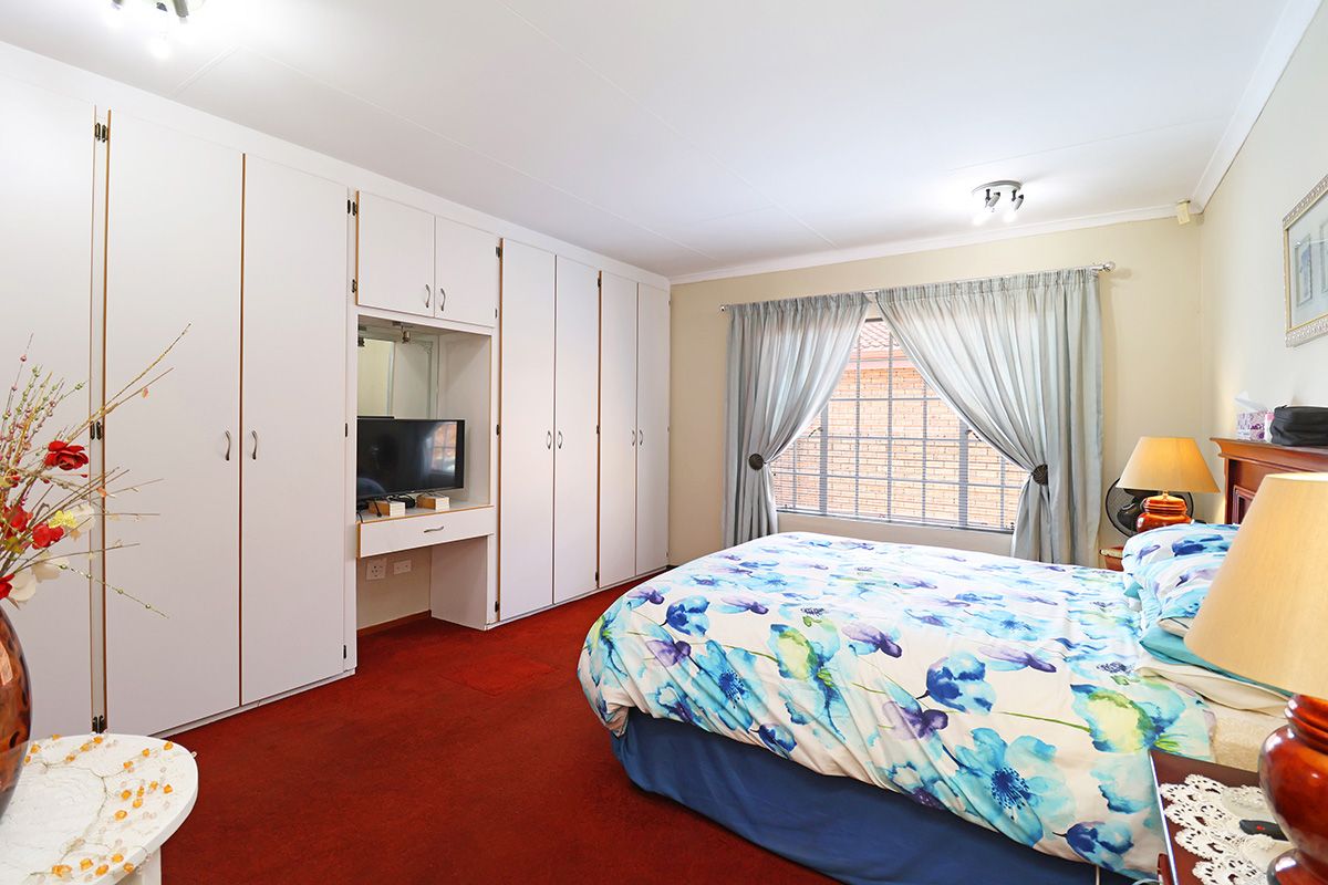 A bedroom featuring extensive built-in cupboards with an integrated vanity area, carpeted flooring, and a window fitted with security bars.