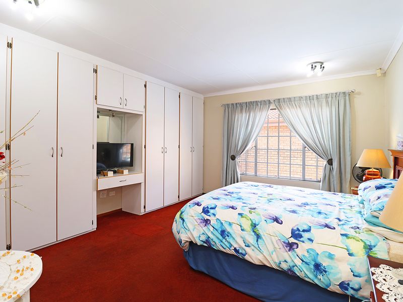 A bedroom featuring extensive built-in cupboards with an integrated vanity area, carpeted flooring, and a window fitted with security bars.