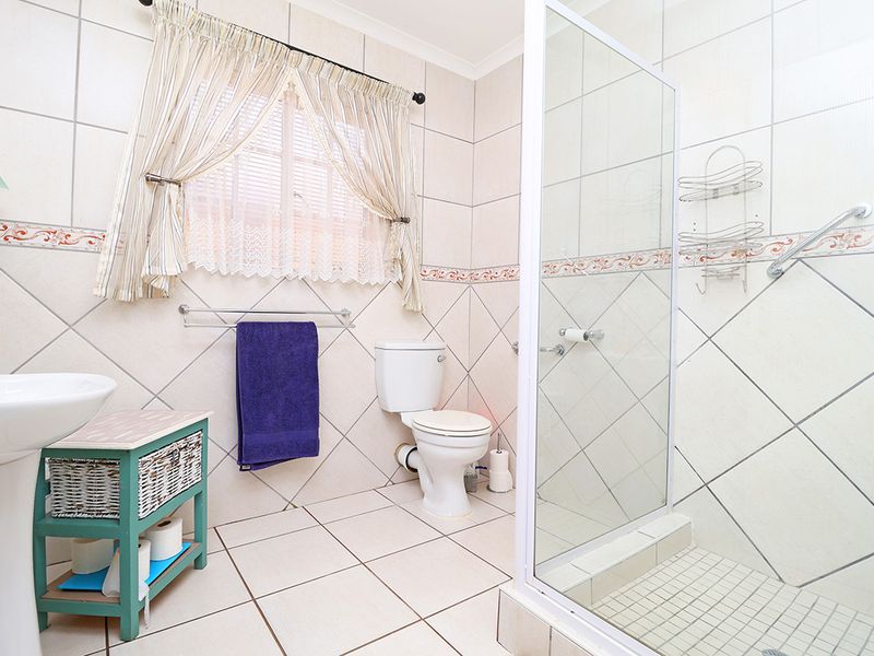 A functional bathroom featuring a pedestal basin, toilet, and a glass-enclosed shower with neutral wall and floor tiling.