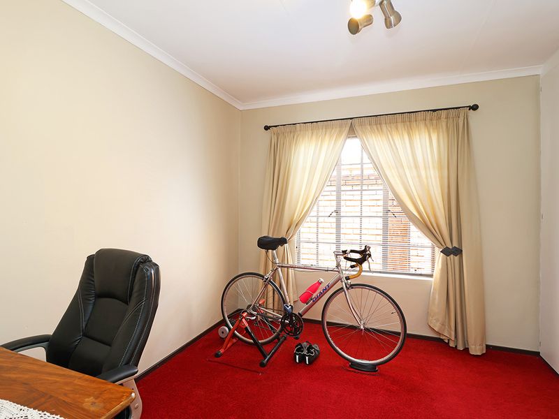 A bedroom featuring built-in cupboards, red carpeting, and a window fitted with security bars.