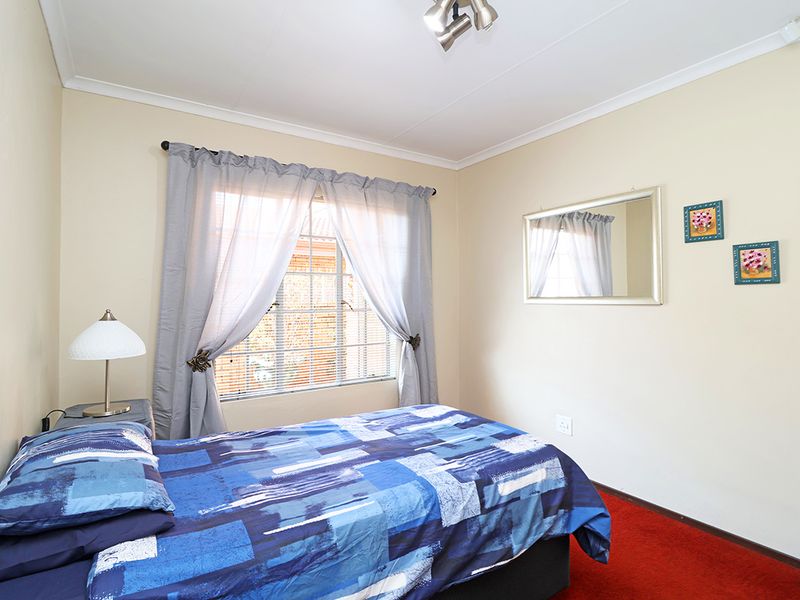 A functional bedroom featuring neutral walls, red carpeting, and a window fitted with security bars and curtains.
