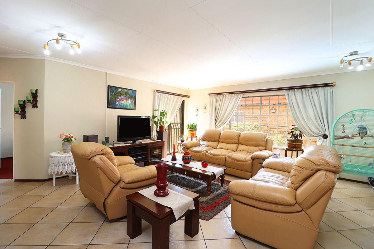 A spacious living room featuring tiled flooring, neutral walls, and large windows with security bars, providing a comfortable and functional family area.
