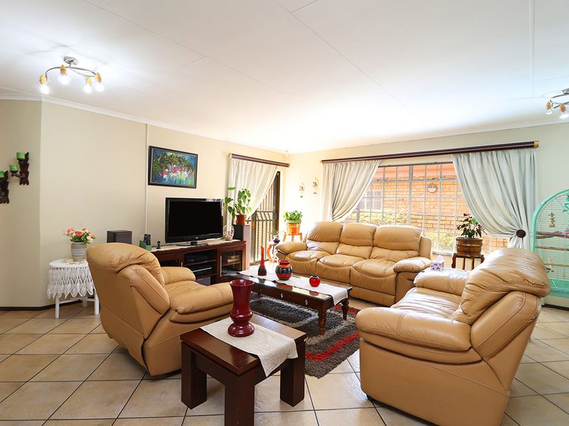 A spacious living room featuring tiled flooring, neutral walls, and large windows with security bars, providing a comfortable and functional family area.