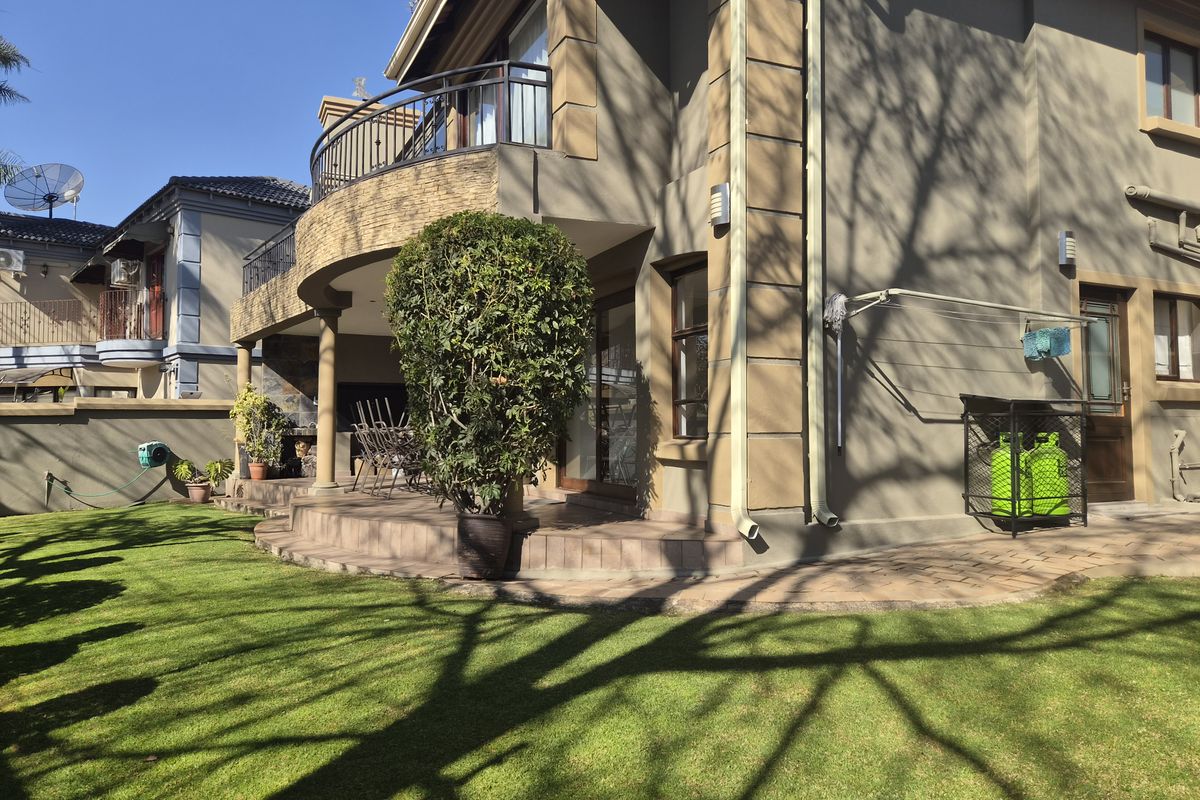 Rear view of the property featuring a covered patio, an upper-level balcony with metal railings, stone facade accents, and a well-maintained garden area.