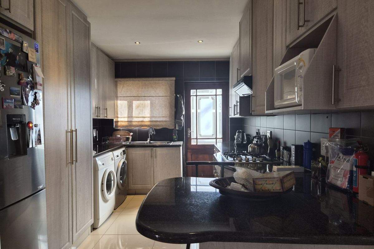 A functional galley-style kitchen featuring light wood-finish cabinetry, dark granite countertops, a gas hob, and integrated laundry appliances.