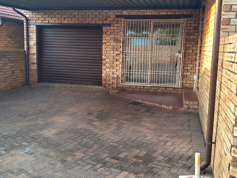 Front exterior view of a townhouse featuring a paved driveway, a single roller garage door, and a secure entrance with a metal security gate.