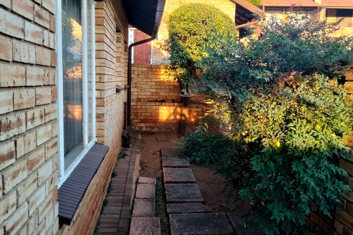 A side garden area featuring a brick facade, paved walkway, and established boundary wall, offering a private outdoor space for the townhouse.