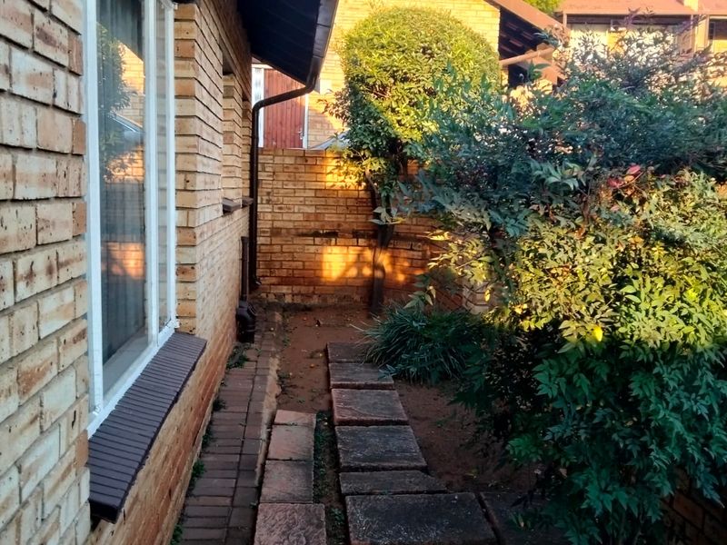 A side garden area featuring a brick facade, paved walkway, and established boundary wall, offering a private outdoor space for the townhouse.