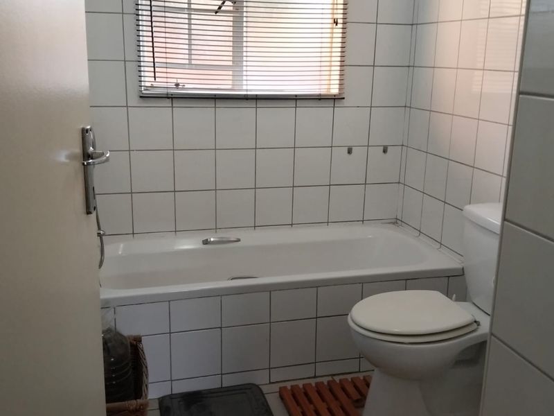 A functional bathroom featuring a standard bathtub, toilet, and white wall tiling, offering a blank canvas for potential modernization and renovation.