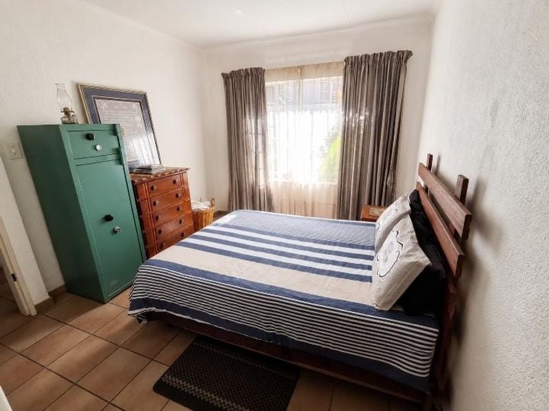 A functional bedroom featuring tiled flooring and large windows with curtain rails, providing a neutral space ready for personalization.