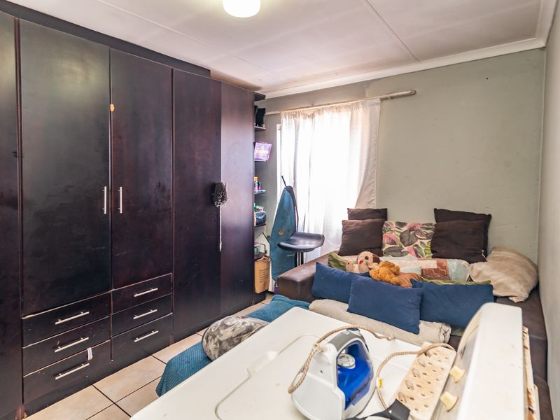 A bedroom featuring built-in dark wood cupboards and tiled flooring, requiring cosmetic updates to improve the overall aesthetic and condition.