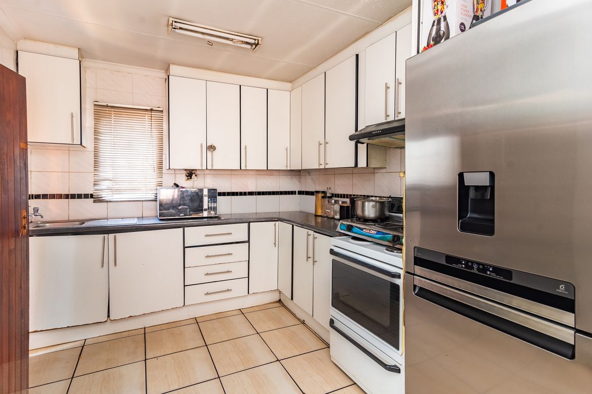 Functional kitchen featuring white cabinetry, tiled backsplash, ceramic flooring, and integrated workspace with a built-in oven and extractor fan.