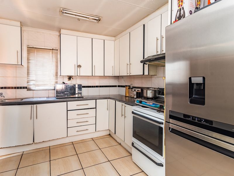 Functional kitchen featuring white cabinetry, tiled backsplash, ceramic flooring, and integrated workspace with a built-in oven and extractor fan.