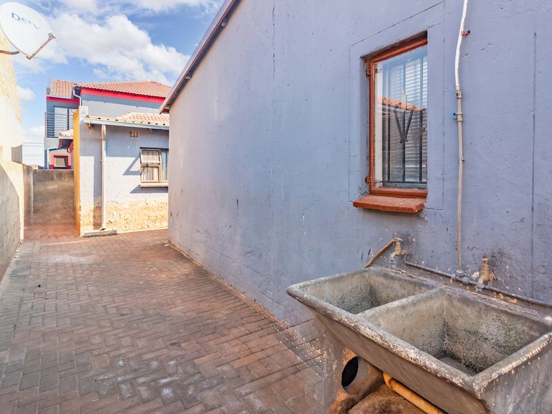 A paved rear courtyard area featuring a double concrete laundry trough, external water taps, and security-barred windows on the exterior wall.