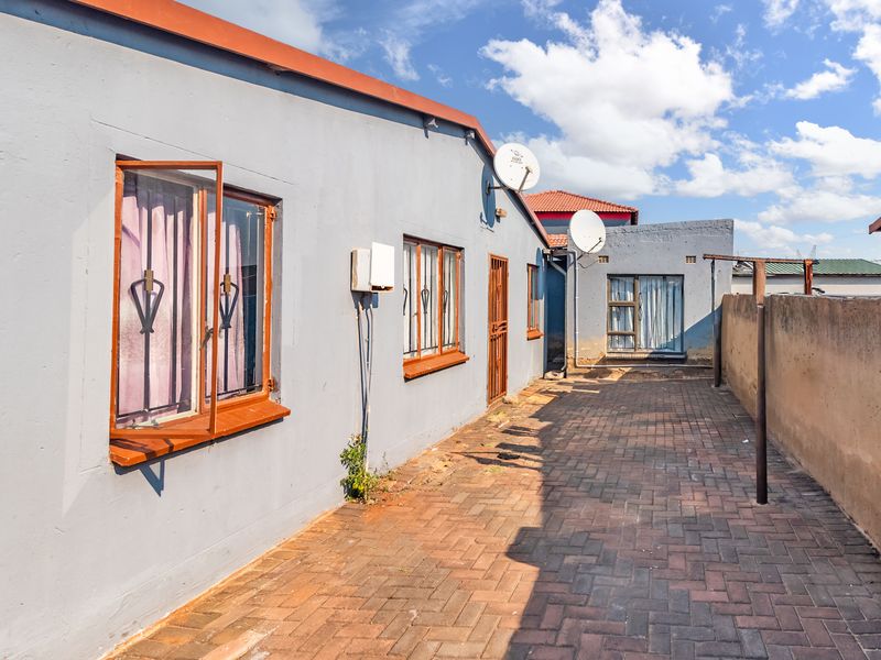 A paved rear courtyard area featuring a boundary wall, security bars on windows, and external satellite dish installations.