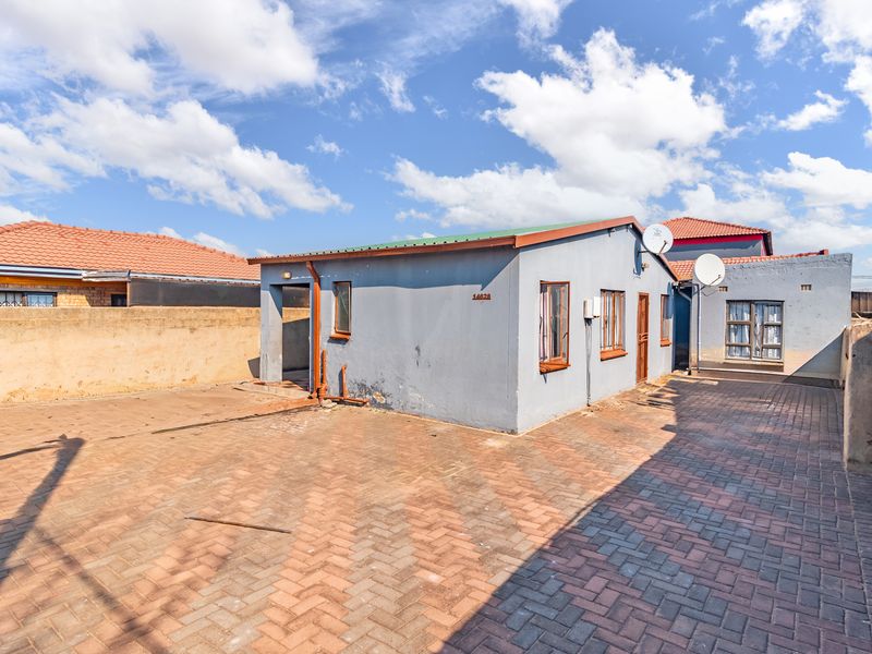 Rear exterior view of the property featuring a paved courtyard, boundary walls, and a single-story structure with a tiled roof.