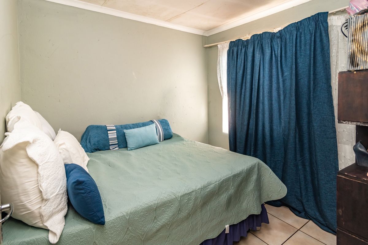 A compact bedroom featuring tiled flooring and a window with curtain rails. The room requires cosmetic updates to the ceiling and wall finishes.