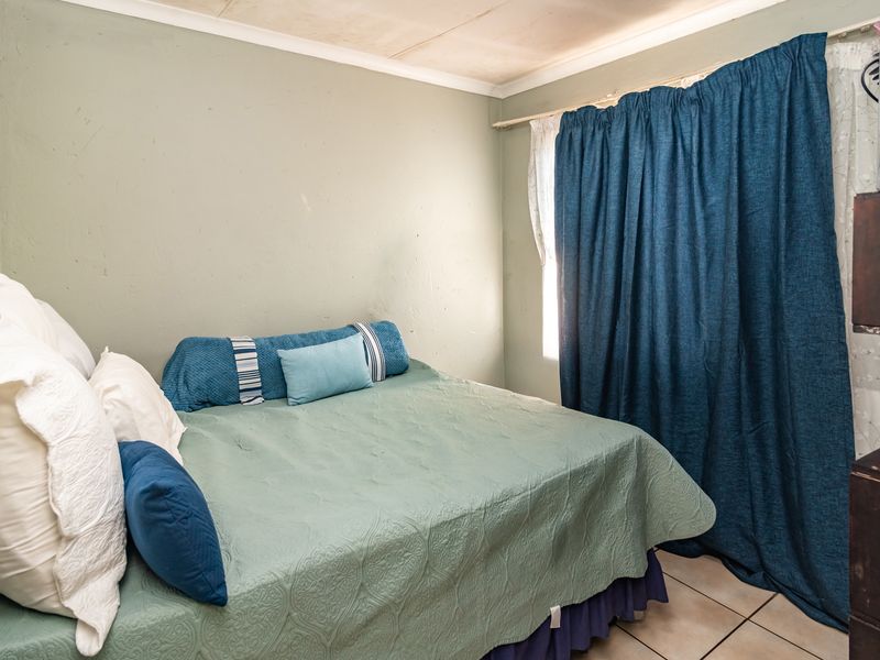 A compact bedroom featuring tiled flooring and a window with curtain rails. The room requires cosmetic updates to the ceiling and wall finishes.