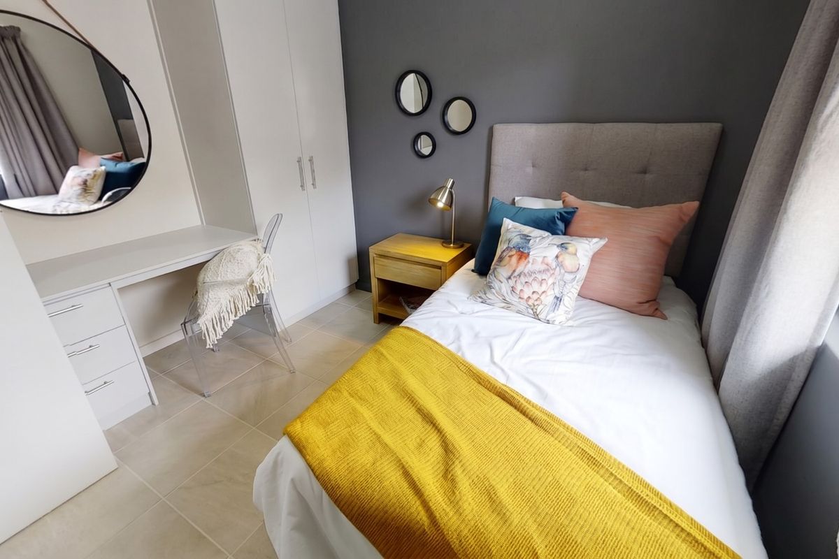 A well-maintained bedroom featuring built-in cupboards, a integrated desk area, and neutral tiled flooring.