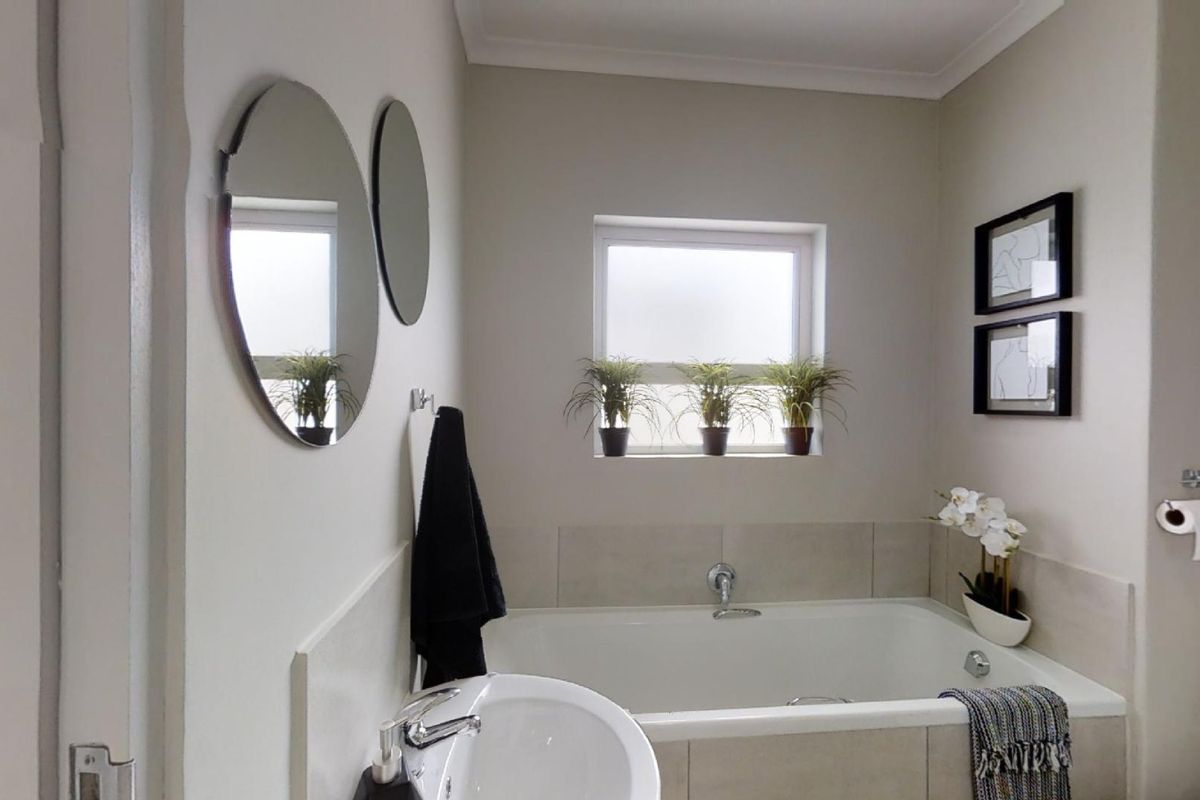 A clean and well-maintained bathroom featuring a built-in bathtub, pedestal basin, and neutral wall finishes with a frosted window for natural light.