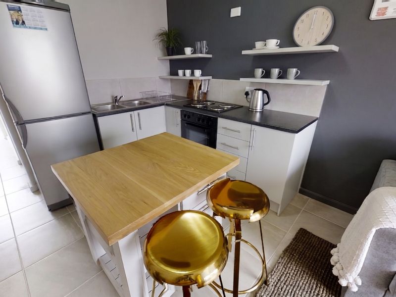Compact modern kitchen featuring built-in oven, hob, stainless steel sink, and floating shelving with a neutral tiled finish.
