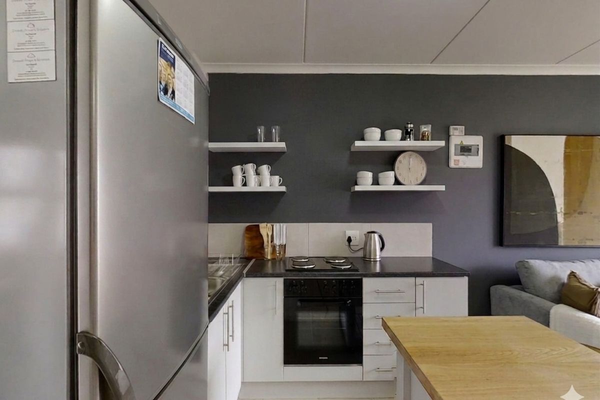 Compact kitchen featuring white cabinetry, dark countertops, built-in oven, electric hob, and floating wall shelves against a dark accent wall.