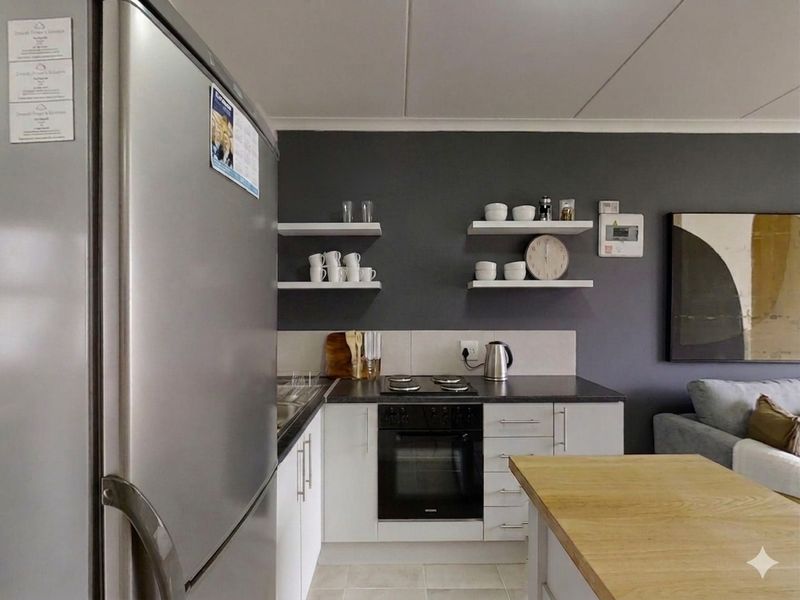 Compact kitchen featuring white cabinetry, dark countertops, built-in oven, electric hob, and floating wall shelves against a dark accent wall.