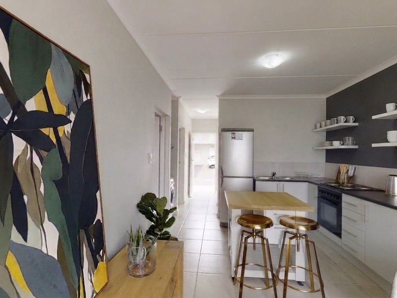 Modern open-plan kitchen featuring sleek cabinetry, floating shelves, and integrated appliances, seamlessly flowing into the living area with tiled flooring throughout.
