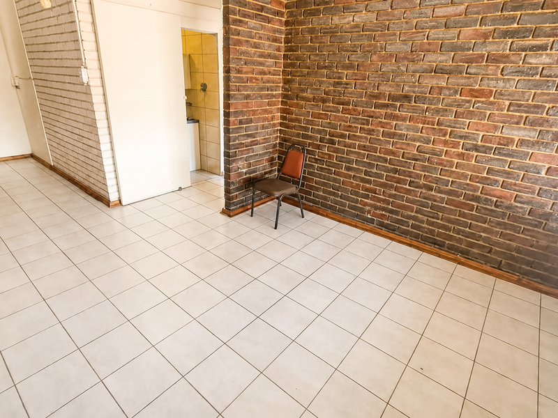 Spacious living area featuring a prominent exposed brick wall, neutral ceramic floor tiles, and natural light through venetian blinds.