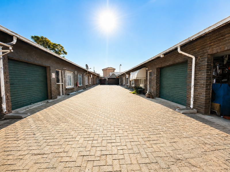 A paved driveway flanked by a row of brick garages with green roller shutter doors and functional guttering systems.
