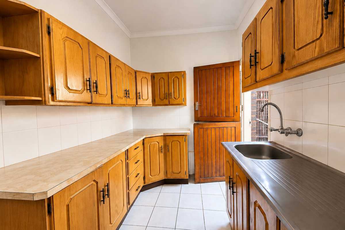 A functional kitchen featuring traditional wooden cabinetry, laminate countertops, a stainless steel sink, and tiled flooring with a classic stable door entrance.