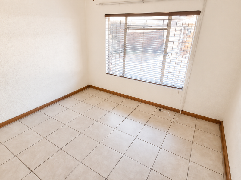 A bright, empty bedroom featuring neutral tiled flooring, clean white walls, and fitted venetian blinds, offering a blank canvas for personalization.