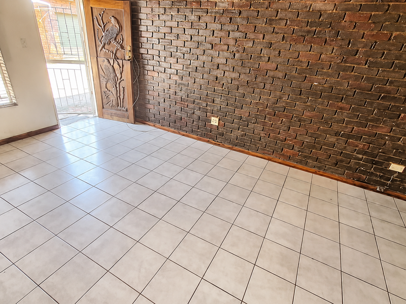 An empty living area featuring a prominent exposed brick wall, ceramic tiled flooring, and a decorative carved wooden entrance door.