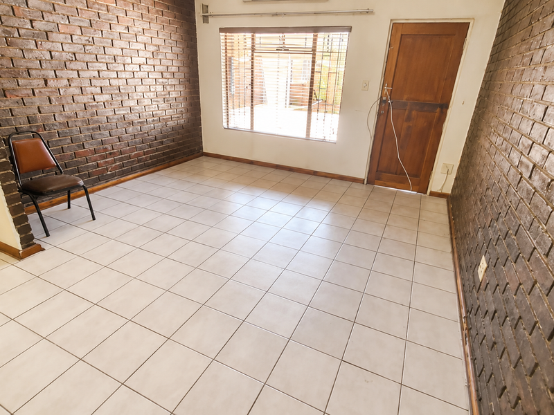 Spacious living area featuring distinctive exposed brick walls, neutral ceramic floor tiles, and direct access to an outdoor space via a timber door.