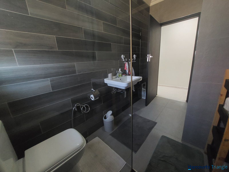 Modern bathroom featuring dark grey tiled walls, a wall-mounted basin, wall-hung toilet, and a glass shower screen.