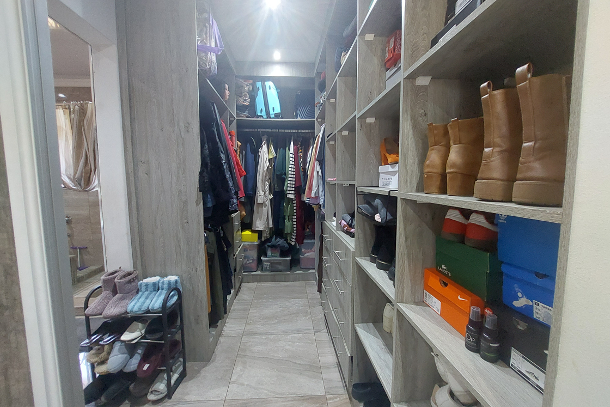 A functional walk-in wardrobe featuring extensive built-in shelving, hanging space, and modern tiled flooring, providing ample storage and organization.