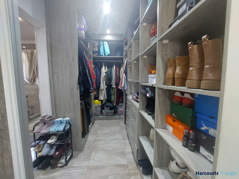 A functional walk-in wardrobe featuring extensive built-in shelving, hanging space, and modern tiled flooring, providing ample storage and organization.