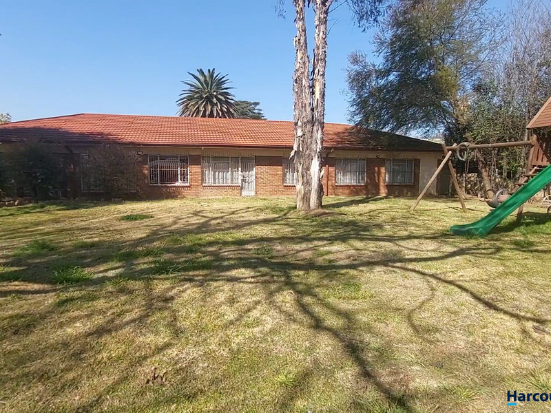 Rear view of a single-story brick house featuring a tiled roof, security bars on windows, and a spacious backyard with a lawn.