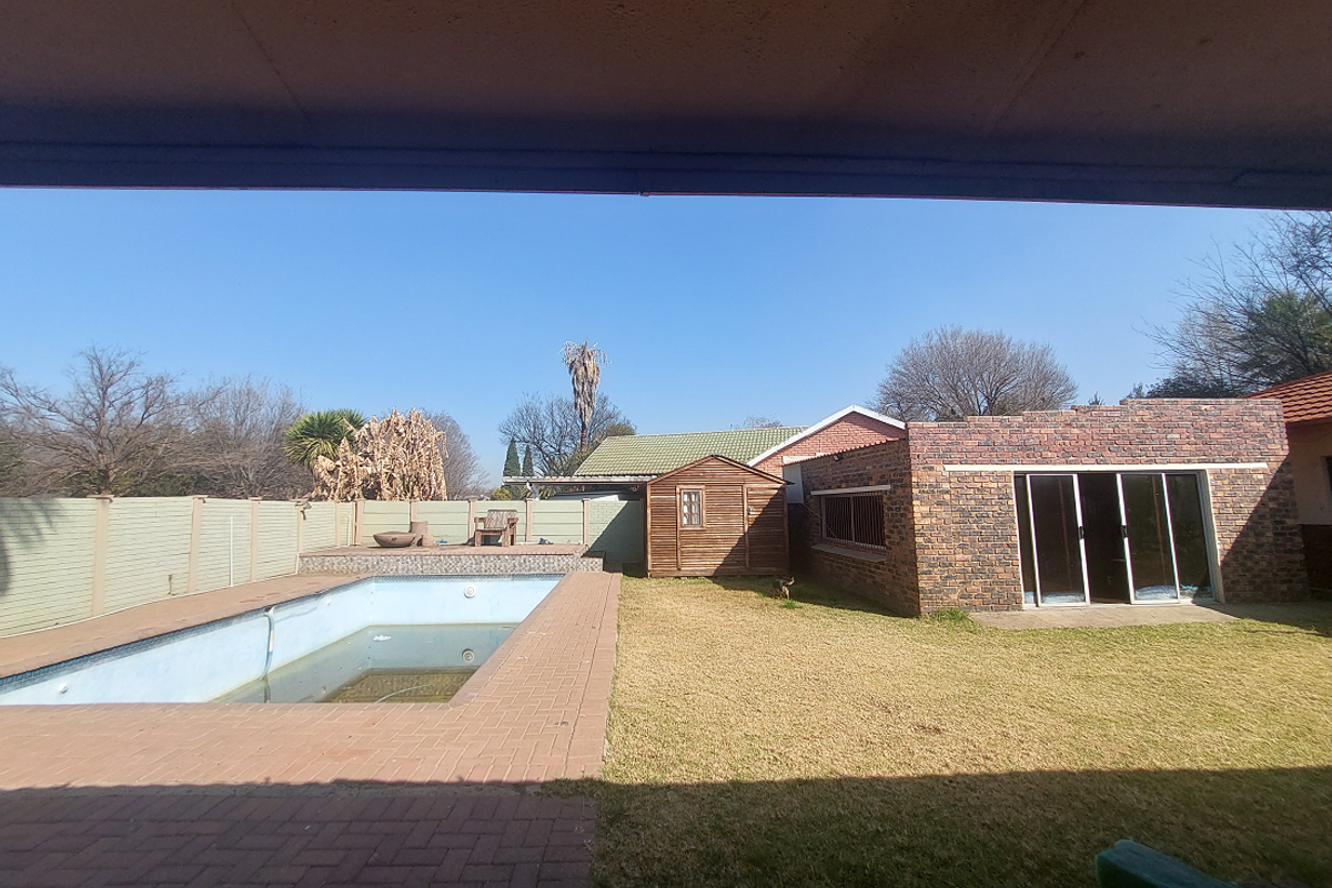 Rear garden view featuring a swimming pool with brick paving, a lawn area, and a detached brick outbuilding with sliding glass doors.
