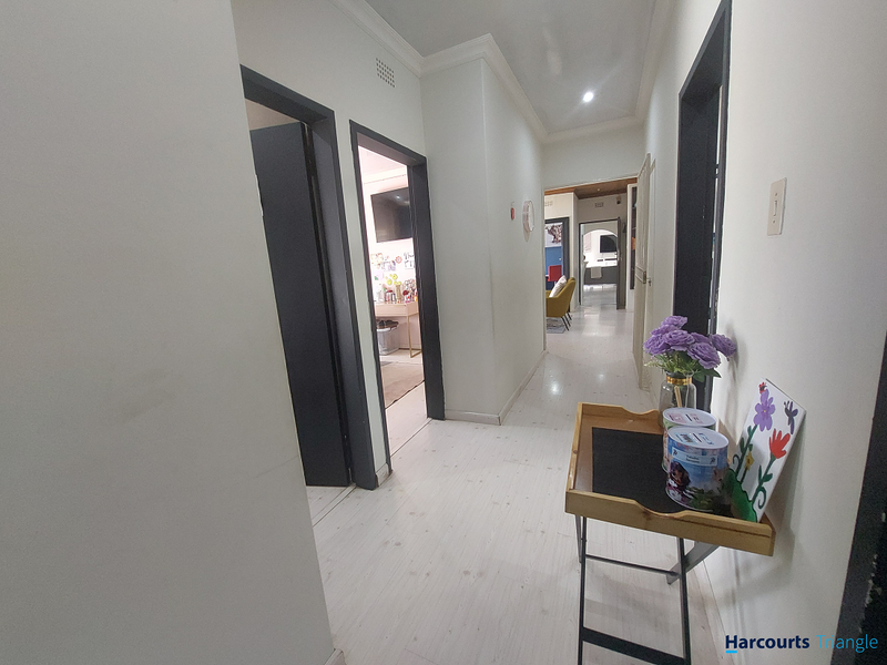A bright, neutral hallway connecting multiple rooms, featuring light-toned laminate flooring, recessed lighting, and clean white walls.