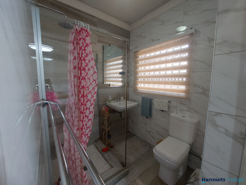 Modern bathroom featuring a walk-in shower with glass screen, wall-mounted basin, and dual-flush toilet, finished with marble-look wall tiles and zebra blinds.