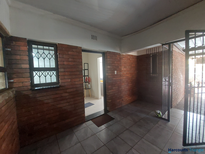 A covered patio area featuring exposed brick walls, tiled flooring, and secure metal gate access to the home interior.