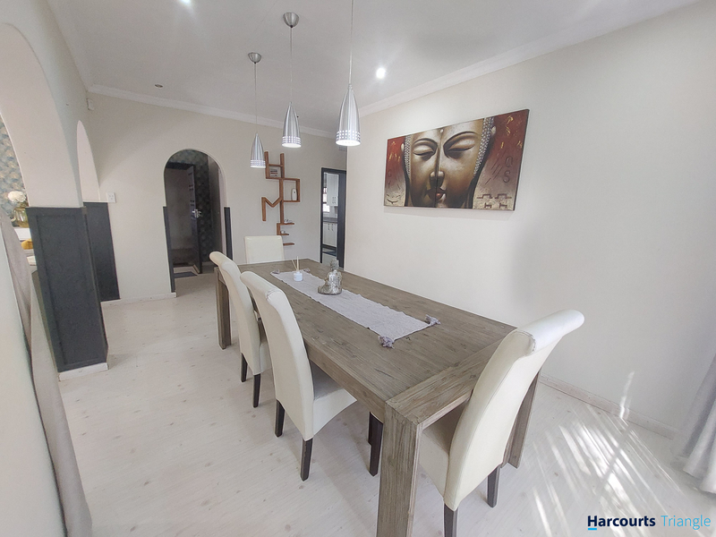 A bright and well-maintained dining room featuring modern pendant lighting, neutral walls, and light-toned laminate flooring with an elegant archway entrance.