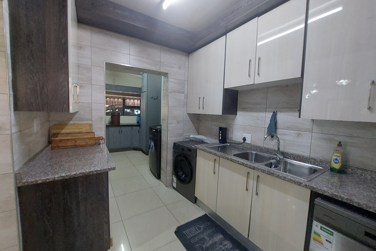 Modern kitchen featuring sleek built-in cabinetry, granite countertops, a double basin sink, and tiled finishes, with an adjacent scullery area.