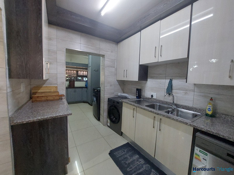 Modern kitchen featuring sleek built-in cabinetry, granite countertops, a double basin sink, and tiled finishes, with an adjacent scullery area.