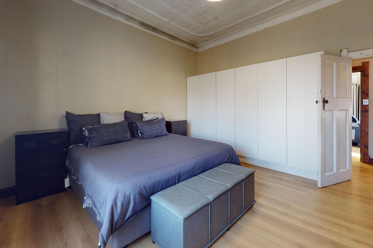 Spacious bedroom featuring laminate flooring, extensive built-in wardrobes, and an ornate ceiling with visible signs of water damage requiring attention.
