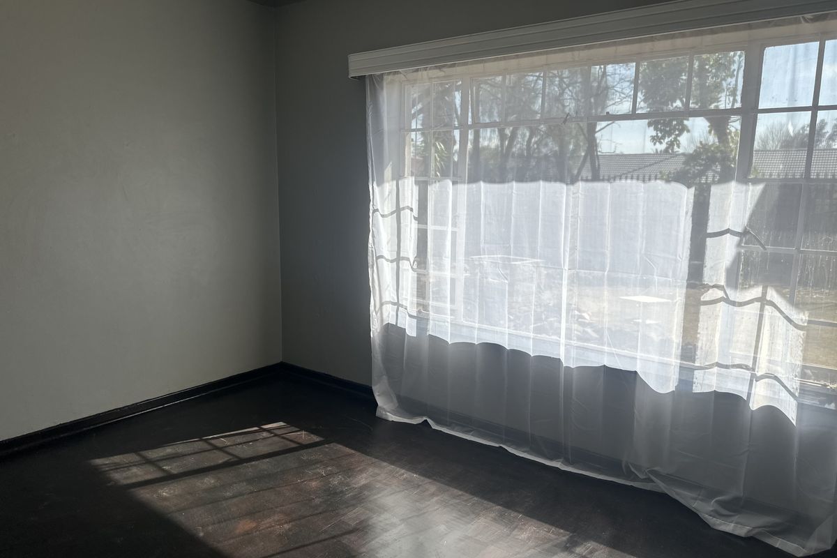 An empty bedroom featuring dark timber flooring, neutral grey walls, and a large window allowing for ample natural light.