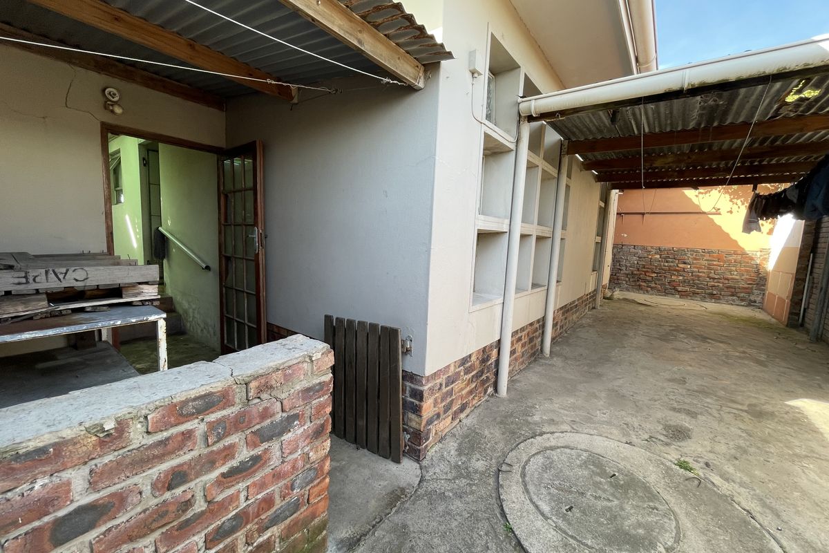 Rear exterior area featuring a paved courtyard, brick boundary wall, and a covered lean-to structure with timber supports.