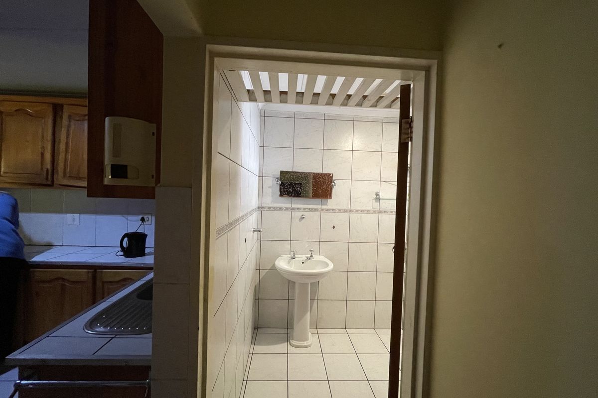 A small bathroom featuring a pedestal basin, fully tiled walls and flooring, and a timber slatted ceiling.